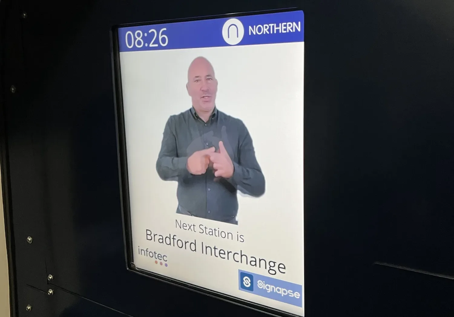 A photo of a screen in a train announcing the next stop is Bradford Interchange, with a video of the announcement in British Sign Language.