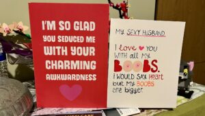 Two valentines day cards. The one on the left says 'I'm so glad you seduced me with your charming awkwardness' and is mostly red with a heart at the bottom; the one on the right says 'My sexy husband, I love you with all my boobs. I would say heart, but my boobs are bigger'.